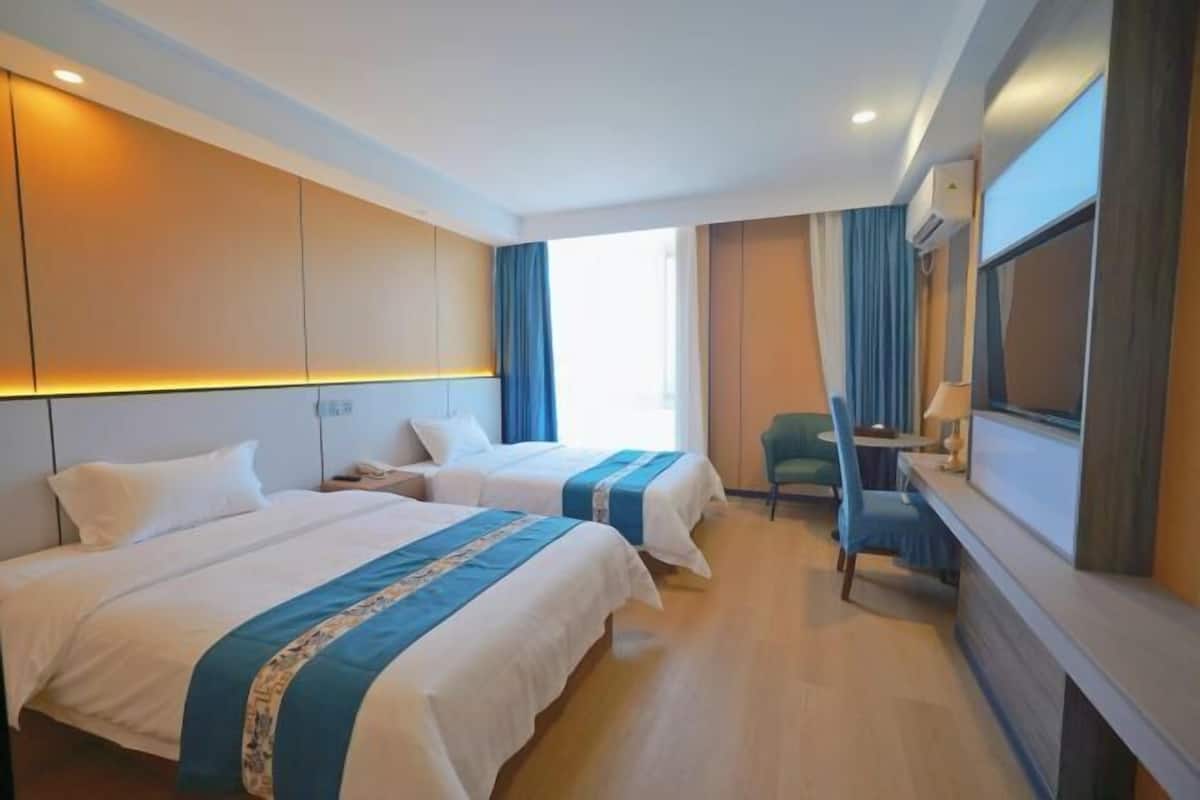 A hotel room with two beds, a desk, a chair, and a TV.