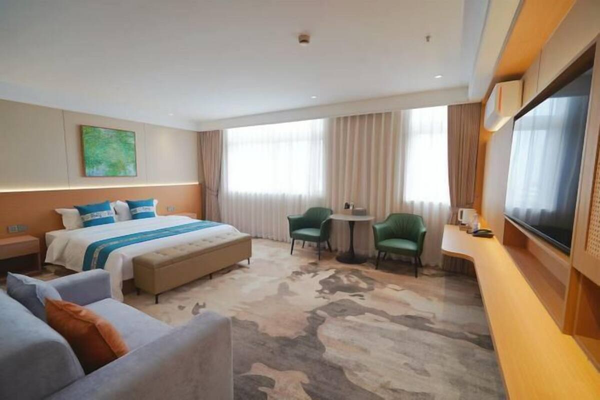A hotel room with a bed, a sofa, a chair, a small table, and a TV.