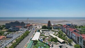 Paisagem costeira urbana com um edifício imponente, um pagode e uma estrada que leva à praia.