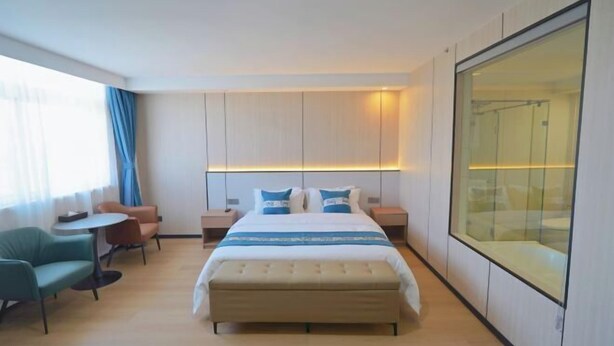 Quarto de hotel com cama, mesas de cabeceira, área de estar com cadeiras, uma pequena mesa e uma janela grande.