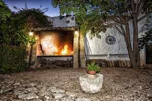 A rustic outdoor fireplace with logs, a stone bench, and a potted plant.