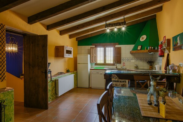 A kitchen with wooden beams, a refrigerator, a sink, and a dining area with a glass table and chairs.