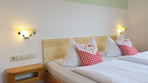 A hotel room with two beds, each with white bedding and red and white checkered pillows. There are wall-mounted light fixtures on either side of the beds.