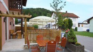 An outdoor seating area with wooden tables and chairs, umbrellas, and a wooden fence.