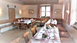 A dining area with long tables set for multiple guests, wooden chairs, and a bench along the wall.