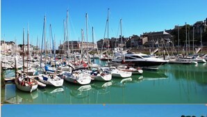 Un port de plaisance où de nombreux bateaux sont amarrés et une plage bondée où les gens profitent de la mer.