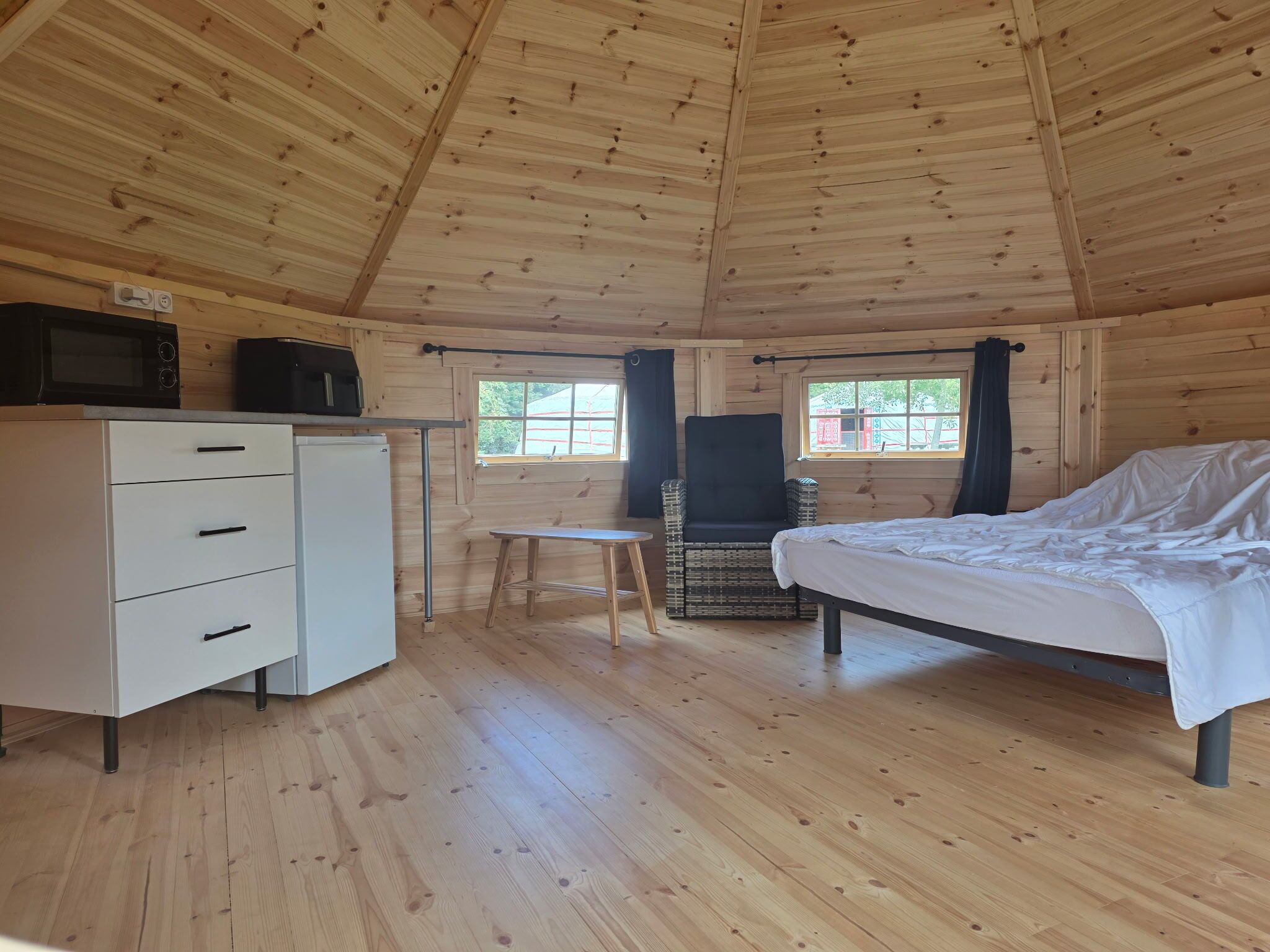A cabin interior with a bed, a small table, a chair, a dresser, and a microwave.