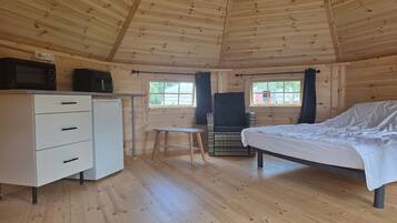 A cabin interior with a bed, a small table, a chair, a dresser, and a microwave.