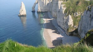 Un paysage côtier caractérisé par de hautes falaises blanches, une plage de sable et une mer d’un bleu limpide.