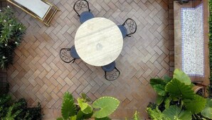 Una mesa redonda al aire libre con cuatro sillas, rodeada por un suelo de ladrillo con patrón de espiga.
