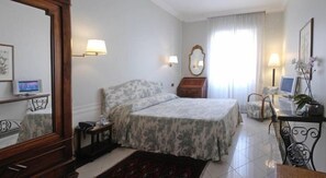Un dormitorio con cama, lámparas de noche, un escritorio con computadora, una silla, un espejo y una ventana con cortinas.