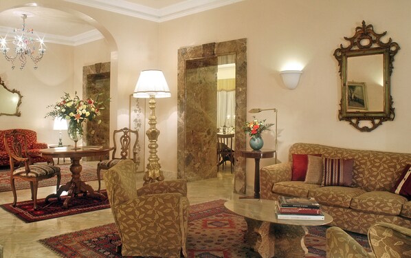 Amplia sala de estar con candelabro, un sofá, sillones, una mesa de centro y un comedor con mesa y sillas.