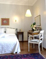 Ein Schlafzimmer mit einem Bett, einem Schreibtisch, einem Stuhl, einer Lampe, einem Spiegel und einem gerahmten Bild an der Wand.