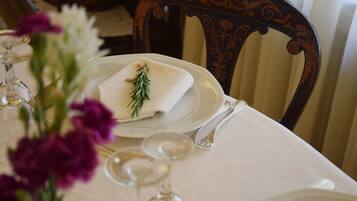 Una mesa de comedor con mantel blanco, una servilleta doblada y una ramita de romero, y una copa de vino.