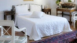 Un dormitorio con cama, mesitas de noche, una silla, escritorio y alfombra.