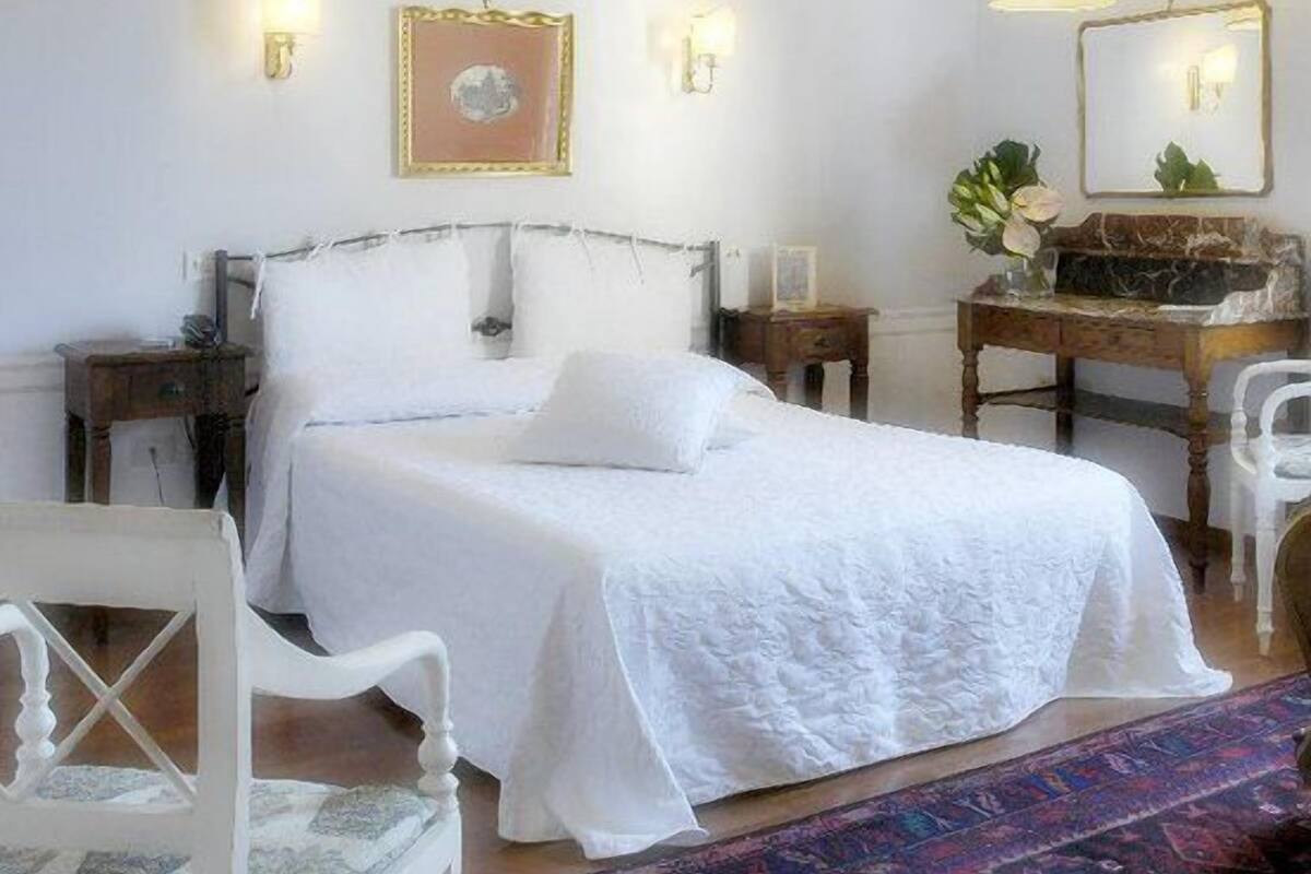 Un dormitorio con cama, mesitas de noche, una silla, escritorio y alfombra.
