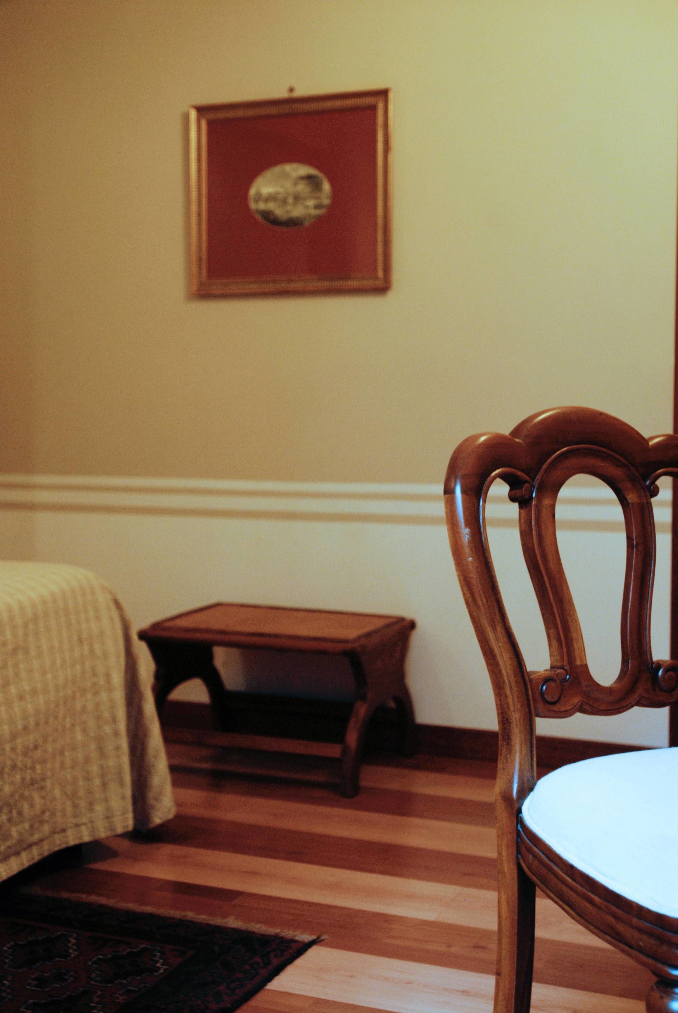 A room with a wooden chair, a small table, and a bed with a patterned bedspread.