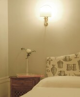 Et soveværelse med et sengebord, en lampe, en vase med en enkelt blomst og en seng med sengegavl med mønster.