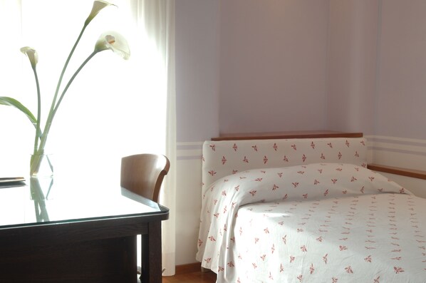 Une pièce comprenant un lit, une chaise et une table sur laquelle est posé un vase de fleurs.