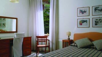 A bedroom with a bed, a desk, a chair, a dresser, a window with curtains, and framed pictures on the wall.