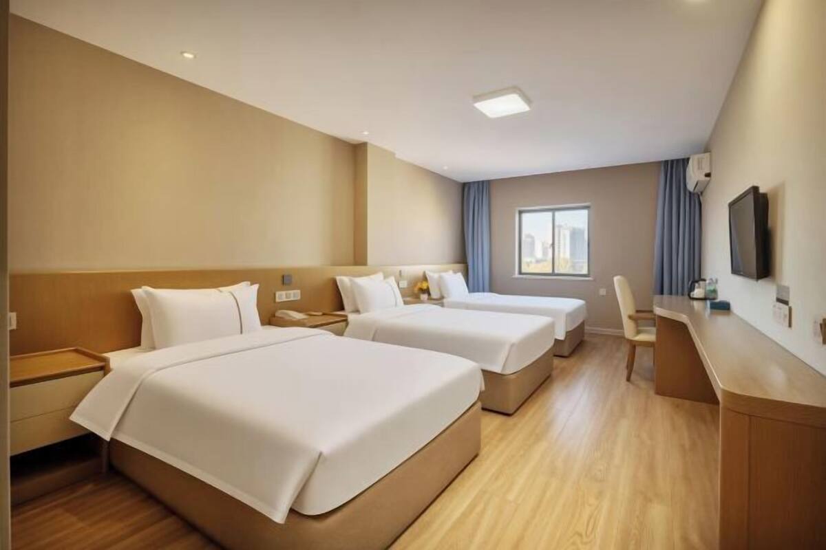 A hotel room with two beds, a desk, a chair, a TV, and a window.