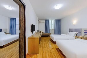Habitación de hotel con dos camas, un escritorio de madera, un televisor de pantalla plana y una mesita pequeña.
