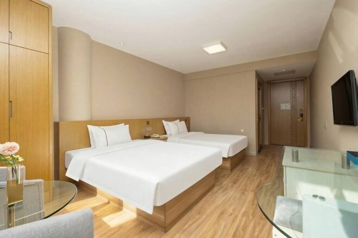 A hotel room with two beds, a glass table, a TV, and a wooden wardrobe.