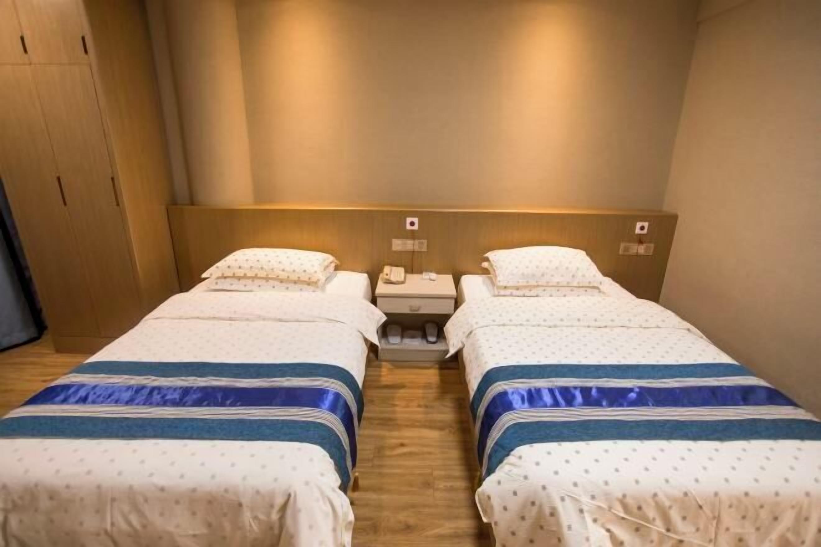 A hotel room with two single beds, wooden flooring, and a nightstand between them.