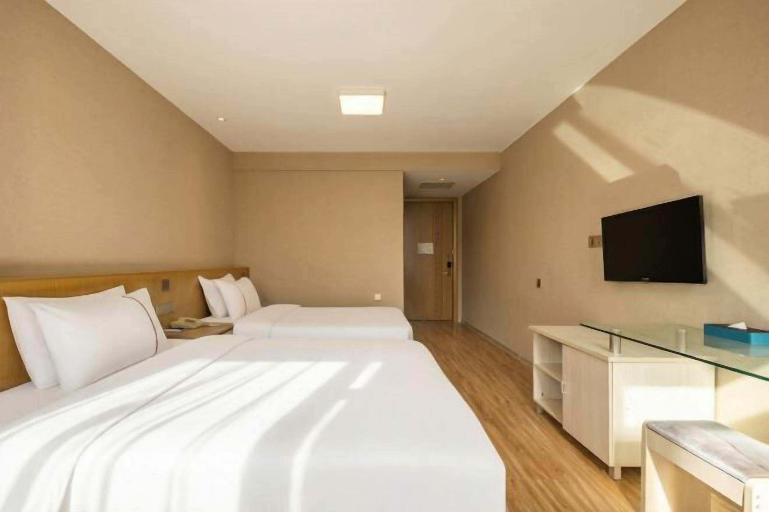 A hotel room with two beds, a flat-screen TV, a glass table, and a wooden floor.