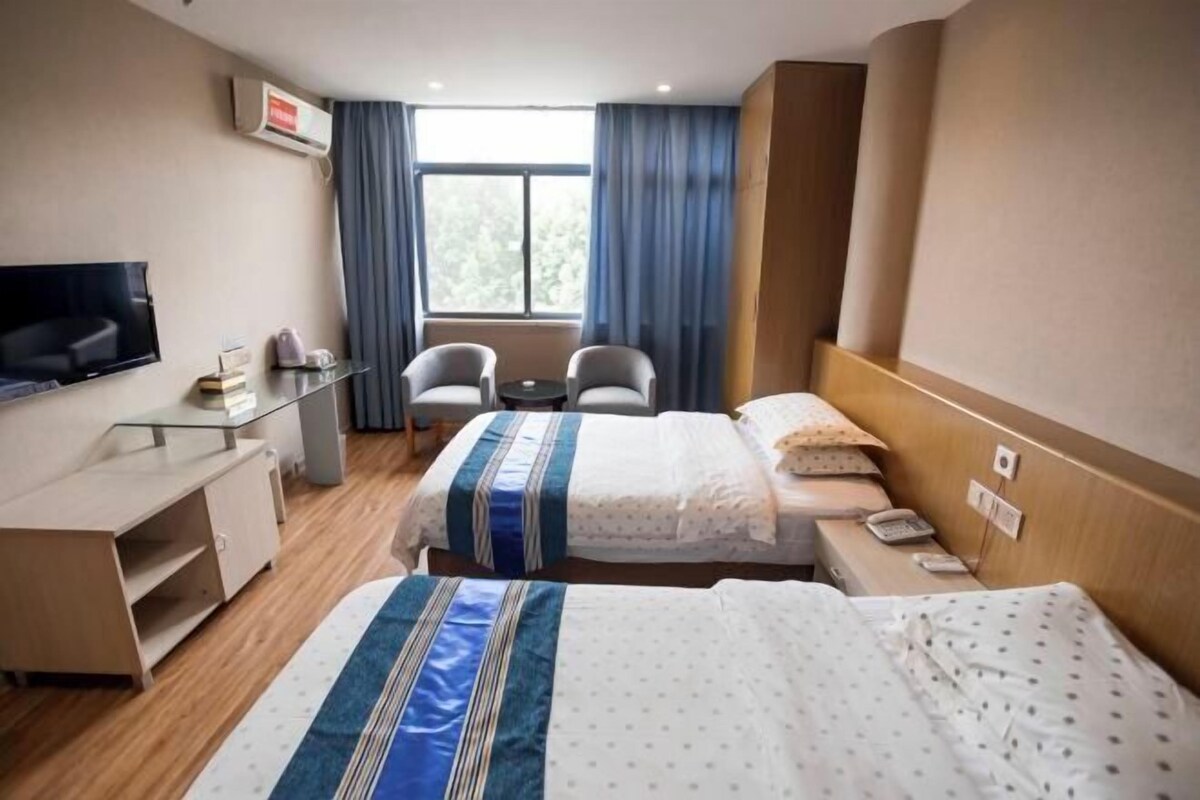 A hotel room with two beds, a desk, a chair, a TV, and a window with curtains.
