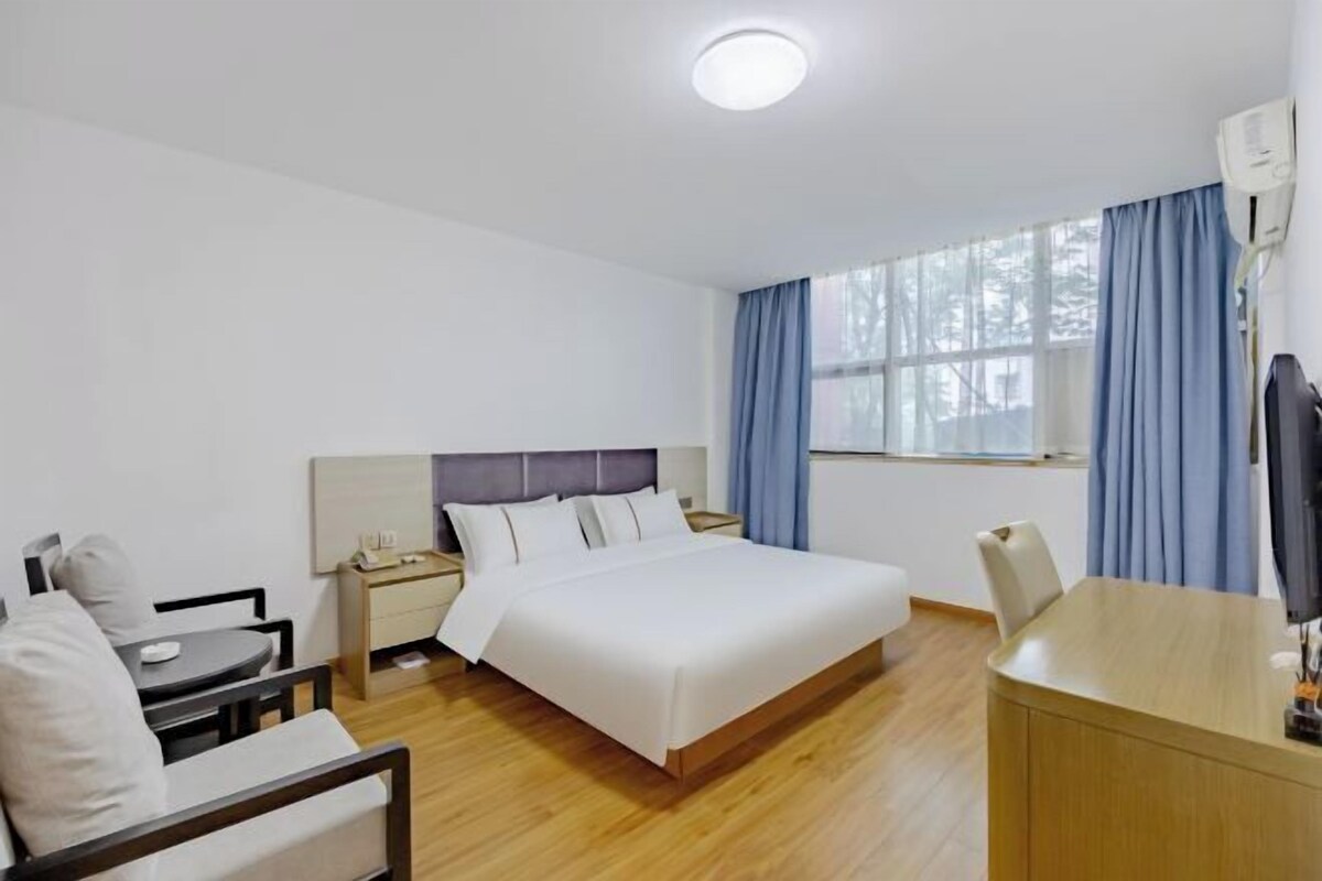 A hotel room with a bed, a desk, a chair, a nightstand, and a window with curtains.