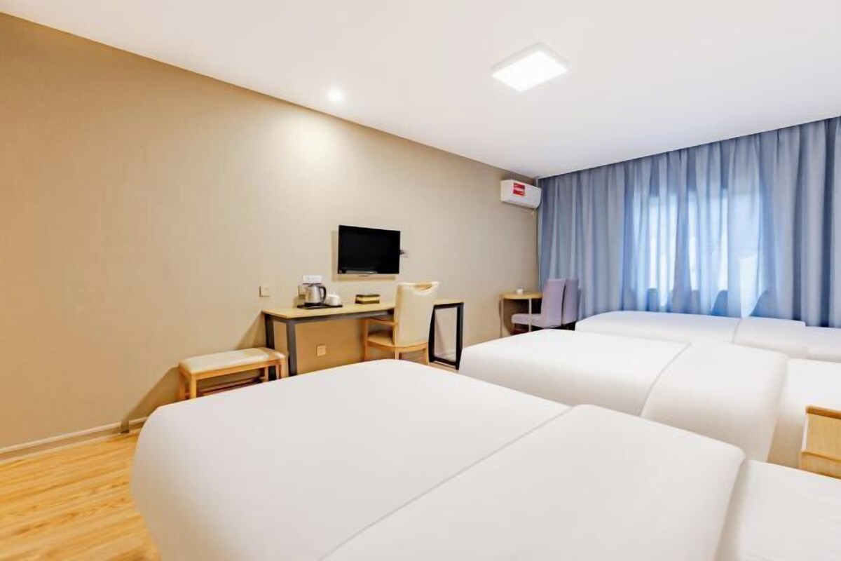 A hotel room with two beds, a desk with a chair, a television, and a window with curtains.
