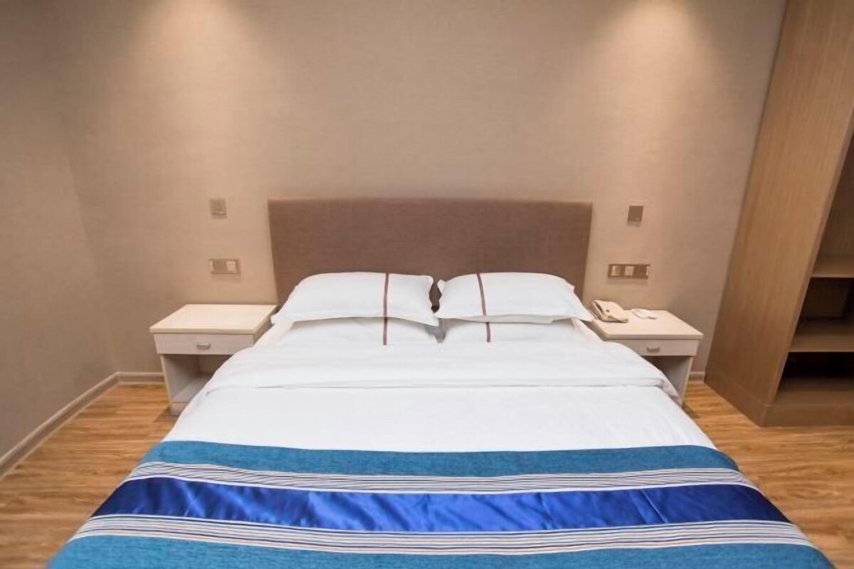 A neatly made bed with a striped bedspread, two bedside tables with lamps, and a wooden floor.