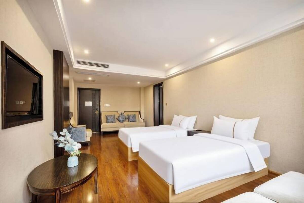 A hotel room with two beds, a sofa, a TV, and a small table with a vase.