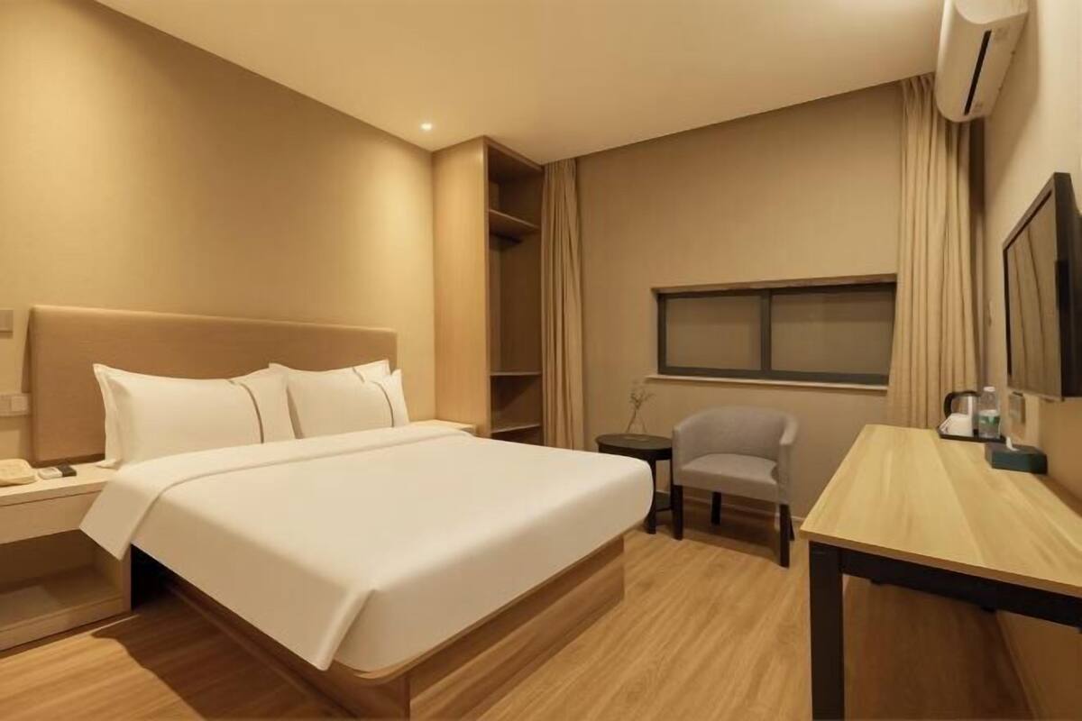 A hotel room with a bed, bedside table, chair, desk, and a window.