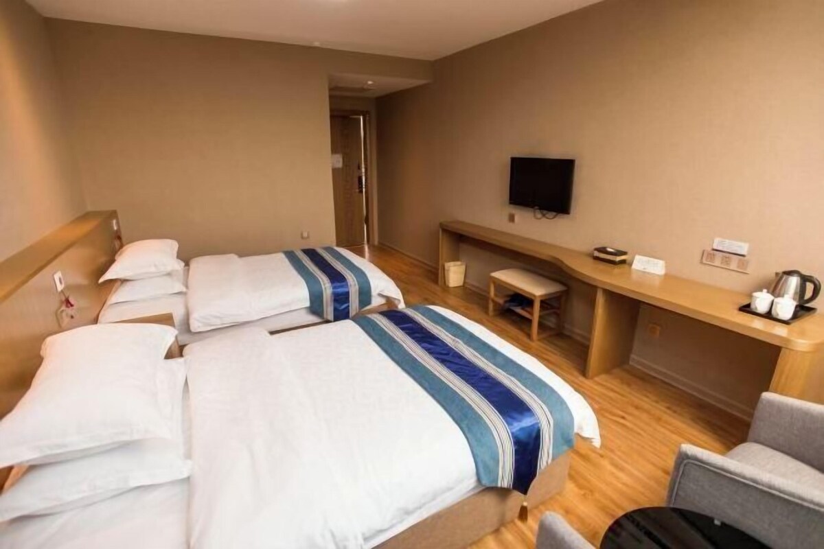 A hotel room with two beds, a desk, a TV, and a seating area.