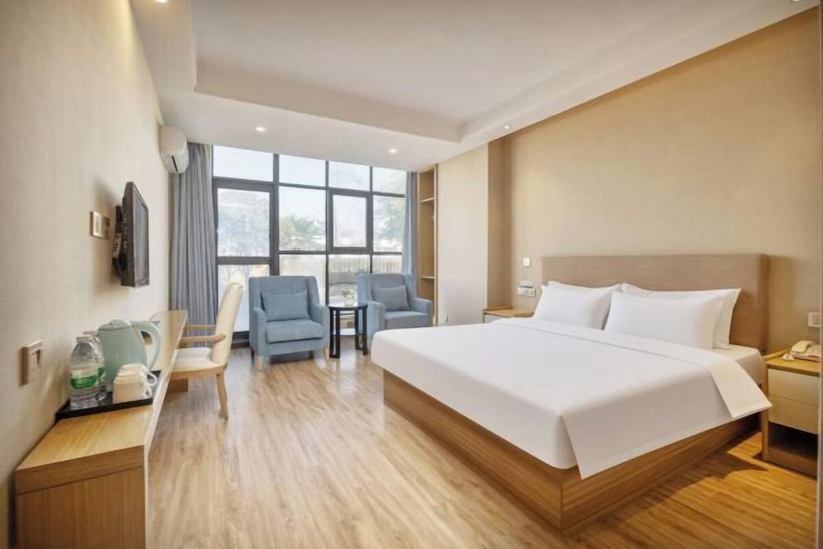 A hotel room with a large bed, a desk with a chair, a small table, and a TV.
