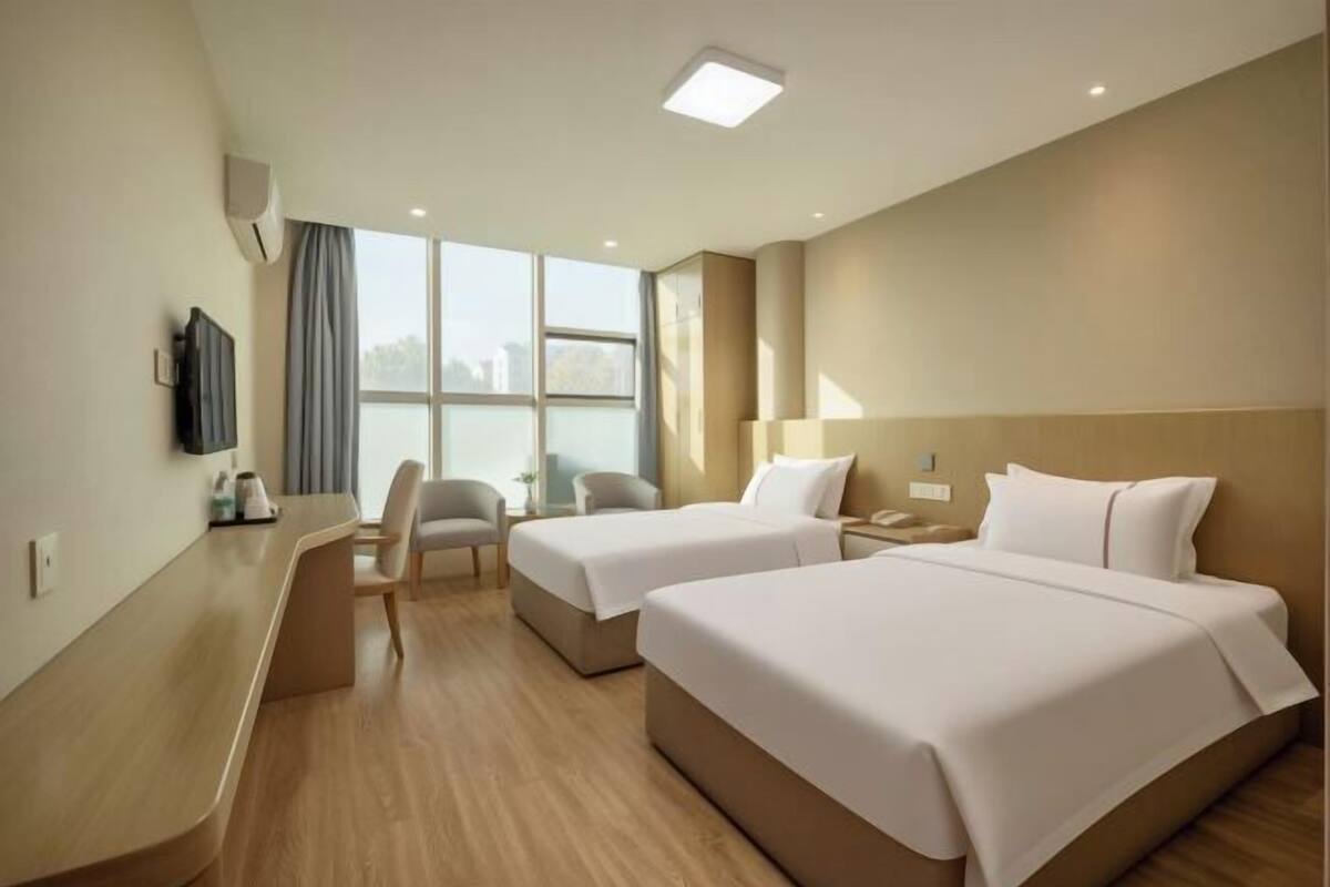 A hotel room with two beds, a desk, a chair, a TV, and a large window.