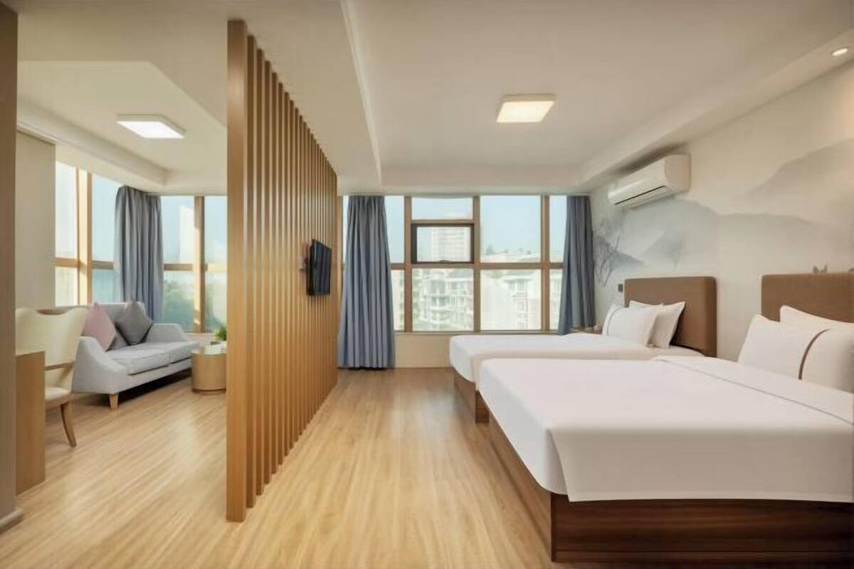 A hotel room with two beds, a sofa, a wooden partition, and large windows.