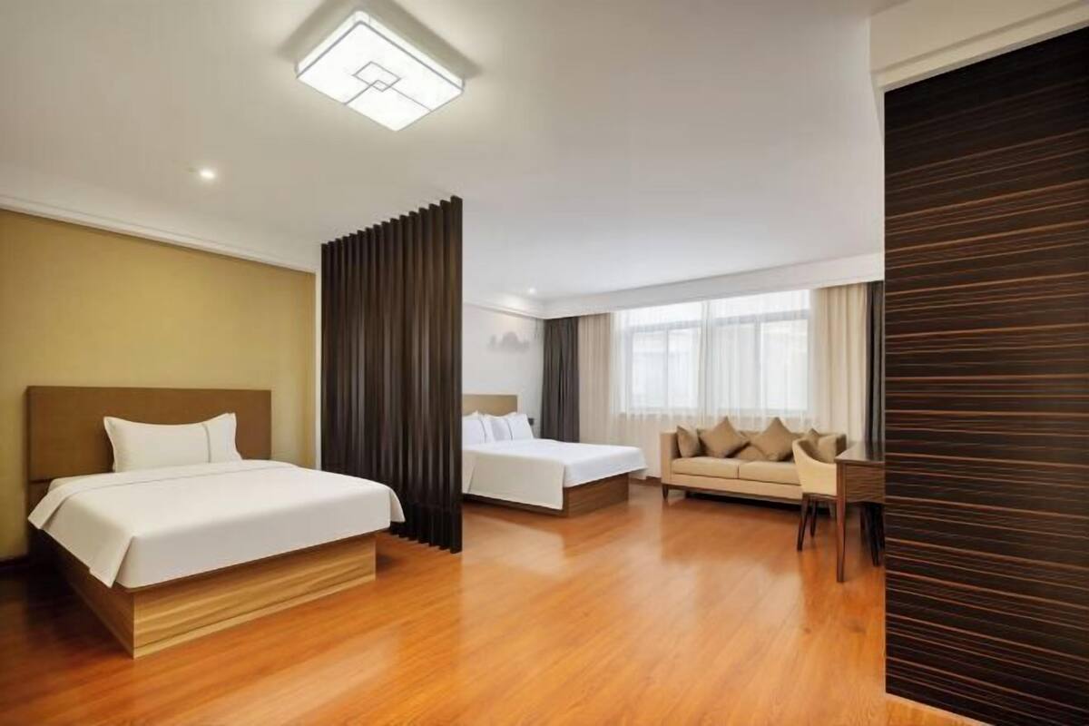 A hotel room with a bed, a sofa, a desk, and a large window.