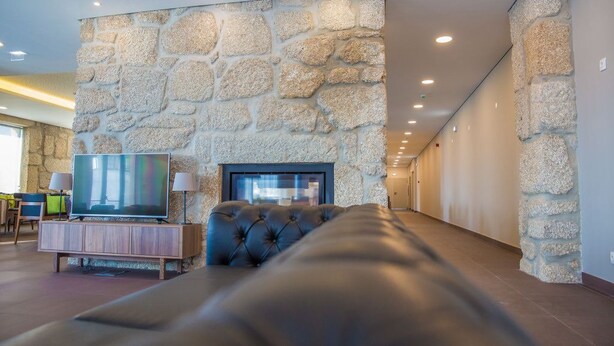 A modern living room with a stone wall, a flat-screen TV, a leather sofa, and a wooden cabinet. - Belmonte Sinai Hotel (Belmonte)