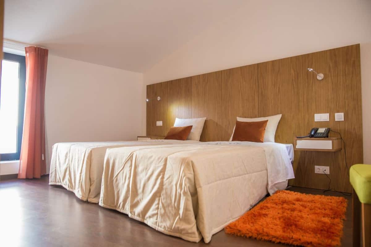 Ein modernes Hotelzimmer mit einem großen Bett, einem Holz-Kopfteil und einem hellen Fenster mit Vorhängen.