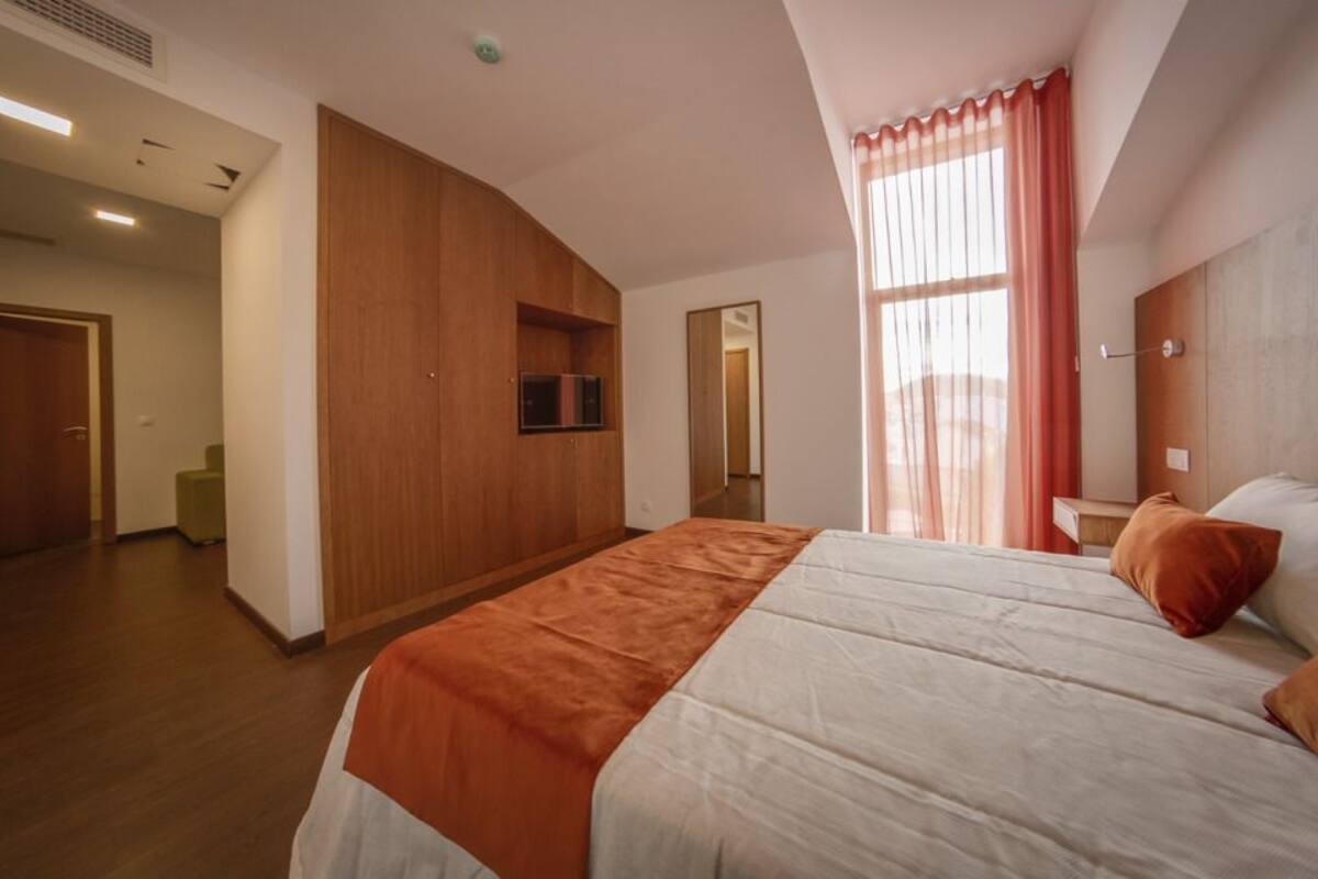 Ein modernes Hotelzimmer mit einem großen Bett, einem an der Wand befestigten Fernseher und einem Fenster mit Vorhängen.