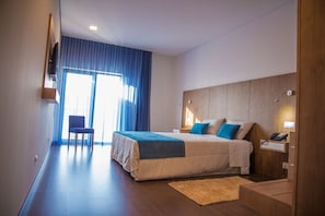 Relax in a serene space with a large bed, desk, and chair, offering a view of the outdoors.