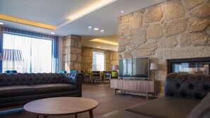 A modern living room with a stone accent wall, a leather sofa, a wooden coffee table, and a flat-screen TV. - Belmonte Sinai Hotel (Belmonte)