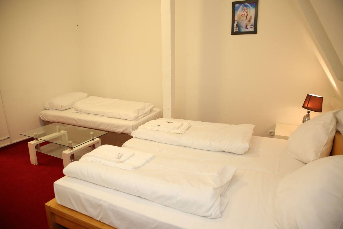 A hotel room with two beds, a glass table, and a lamp.