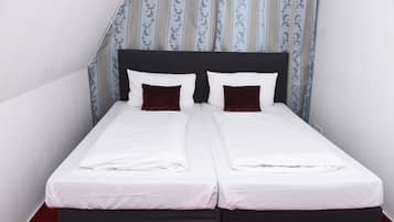 Ein Doppelbett mit weißen Leinentüchern und zwei dunkelroten Kissen, ein schwarzer Kopfteil sowie ein gemustertes Vorhang im Hintergrund.