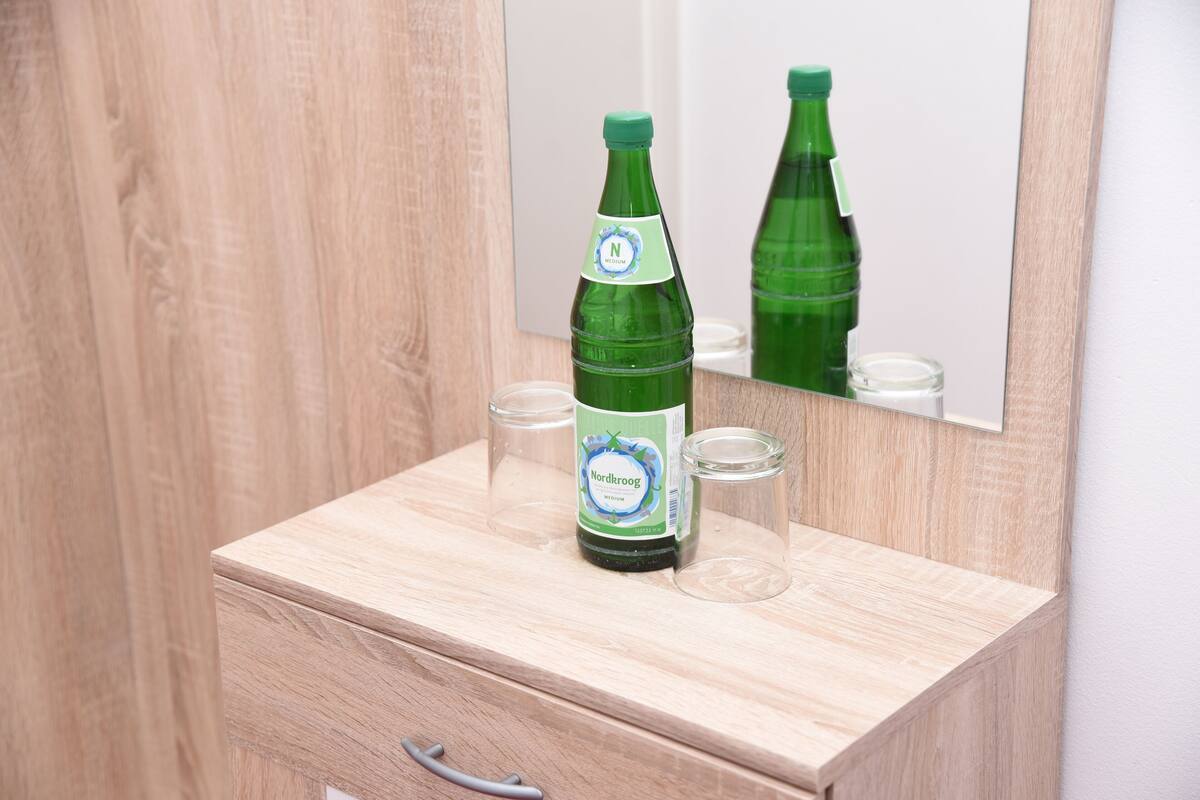 A green bottle of Nordkroog beer on a wooden dresser with a mirror reflecting the bottle.