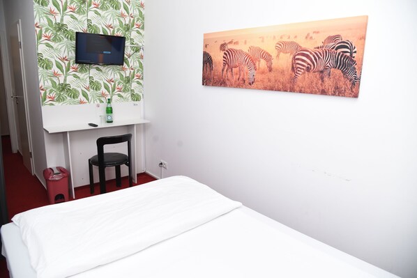 Una habitación de hotel con cama, escritorio, silla, televisor y un cuadro de cebra en la pared.