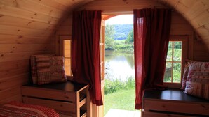 A cozy cabin room with a wooden interior, a window with red curtains, and a view of a lake and greenery outside. - NATURAMA Beilngries (Beilngries)